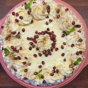 ümmargune kohupiima tort, tagasihoidliku kaunistusega. Kaunistuseks kasutatud vahooore roose, granaatõuna seemneid ja mündilehti