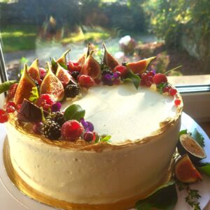 ümmargune vaarika- valge šokolaaditort suvises päikesepaistes. kaunistuseks viigimarjad, põldmarjad ja kuldne toiduvärv