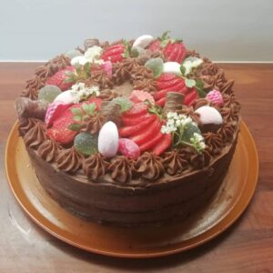 ümmargune šokolaaditort, kaunistatud värskete maasikatega, kommidega ja lilledega