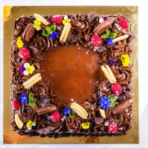 kandiline, rohke šokolaadi kaunistusega tort. kaunistuses šokolaadi lisaks küpsised, marjad, lilled ja mündlehed